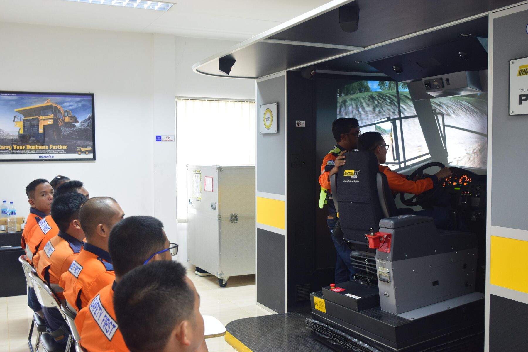 An instructor coaching a trainee in a haul truck simulator while other trainees watch