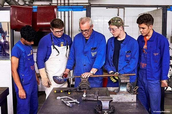An experienced instructor showing apprentices a technique at a workshop vice